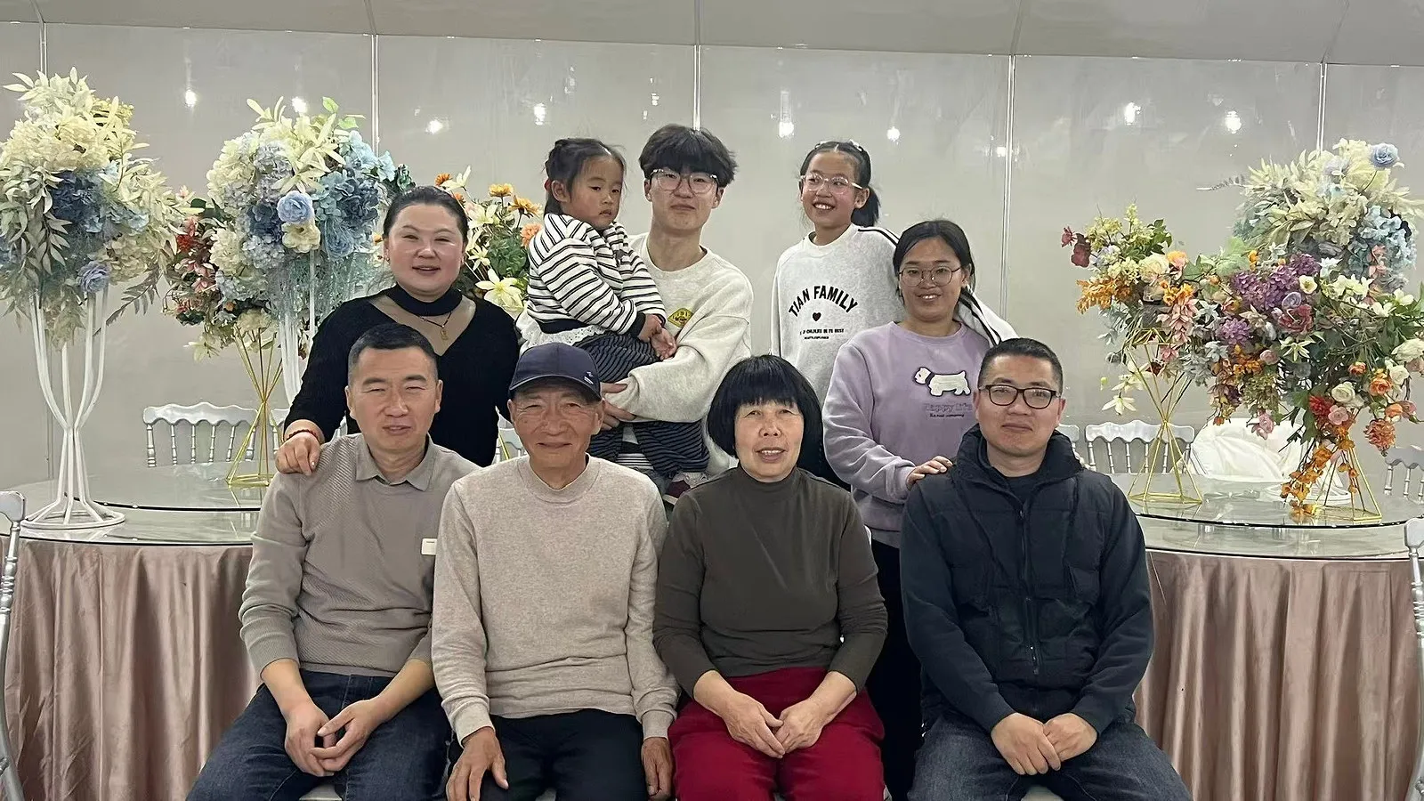 现在的合影:八个人,前排坐着三位长辈,后排站着大人和孩子,两侧是花艺布置